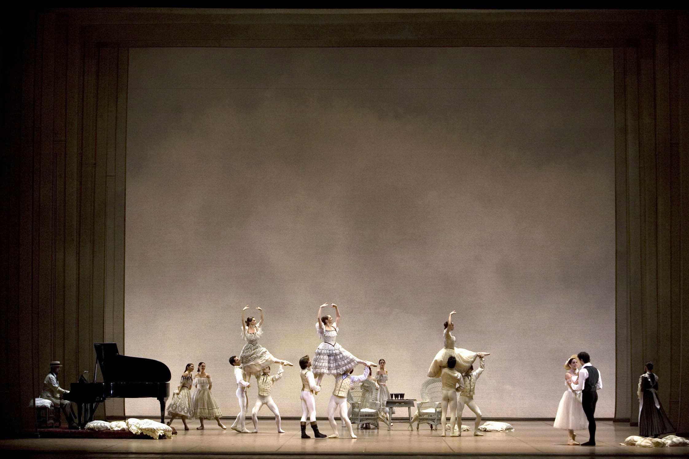 Secondo atto. La scena si svolge presso l’esterno della casa di campagna. Il fondale è di colore beige, con tinte sfumate che ricordano il cielo. A sinistra, un uomo in un elegante completo beige suona un pianoforte a coda, che è appoggiato su una piccola pedana. Al centro della scena, due poltrone e un tavolino, di vimini bianco. Sul tavolino, dei calici di colore nero. A terra sono appoggiati, in ordine sparso, dei grandi cuscini bianchi lavorati all’uncinetto. Al centro del palco, tre coppie di cavalieri sostengono ciascuna una dama in aria, mentre due coppie di dame osservano la scena. Tutti indossano eleganti abiti sui toni del bianco e del beige. All’estrema destra, Armand e Marguerite sono uno di fronte all’altra e si tengono per mano. La donna sorride e indossa un elegante abito beige, che le lascia scoperte le spalle, lungo fino a metà polpaccio. In testa, un cappellino di paglia. Armand indossa il frac ma senza giacca.