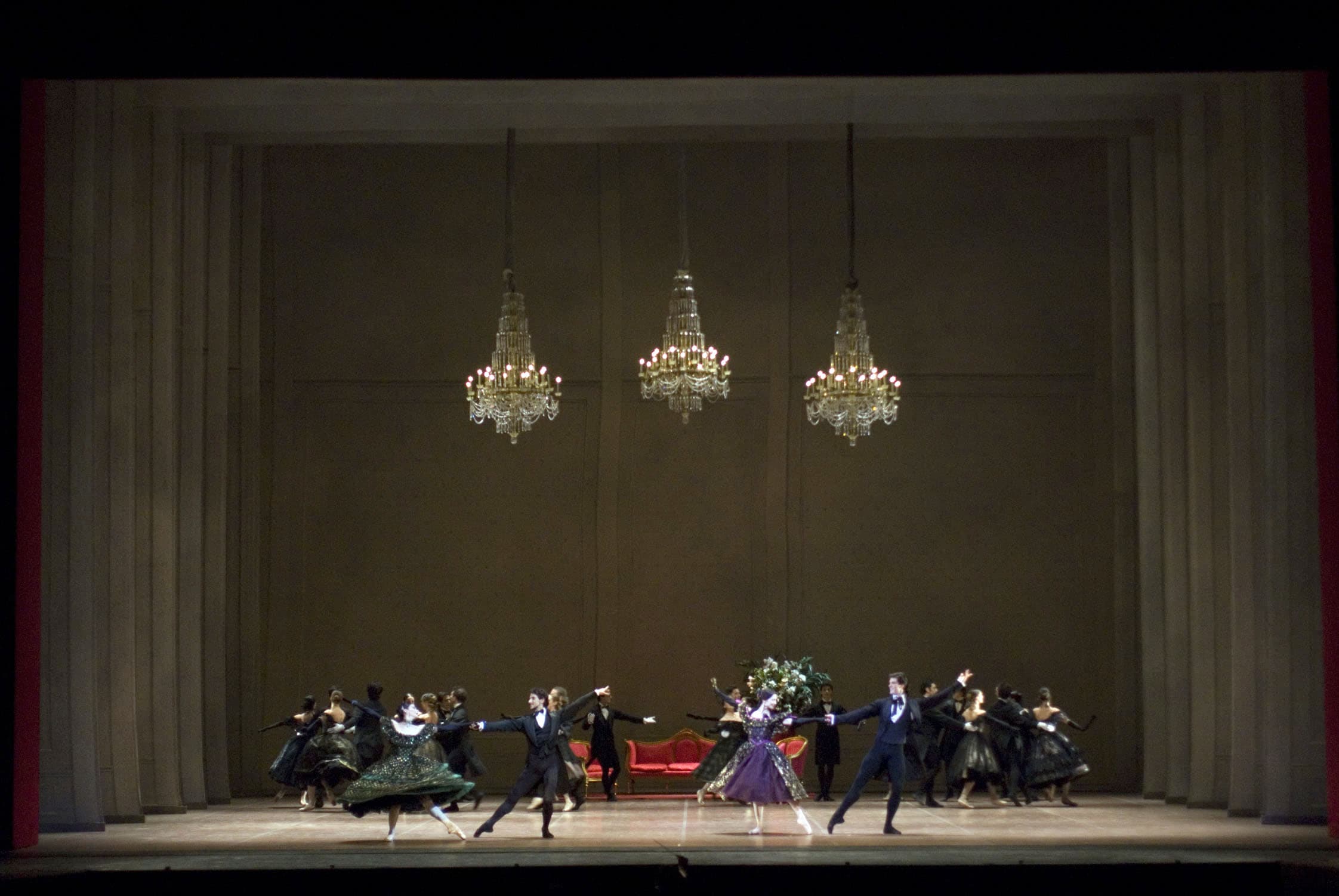Terzo atto. La scena si svolge in una sala da ballo. Il fondale è in tulle, dipinto a simulare una parete con boiserie, mentre dal soffitto scendono tre eleganti lampadari di cristallo. Di fronte al fondale, un divano di colore rosso con rifiniture di colore oro, due poltrone identiche al divano e un tavolino di legno con un grande vaso di fiori. Al centro della scena, le dame e i cavalieri: questi ultimi indossano il frac, mentre le dame eleganti abiti sui toni del verde e del viola, guanti neri lunghi fino al gomito e gioielli.