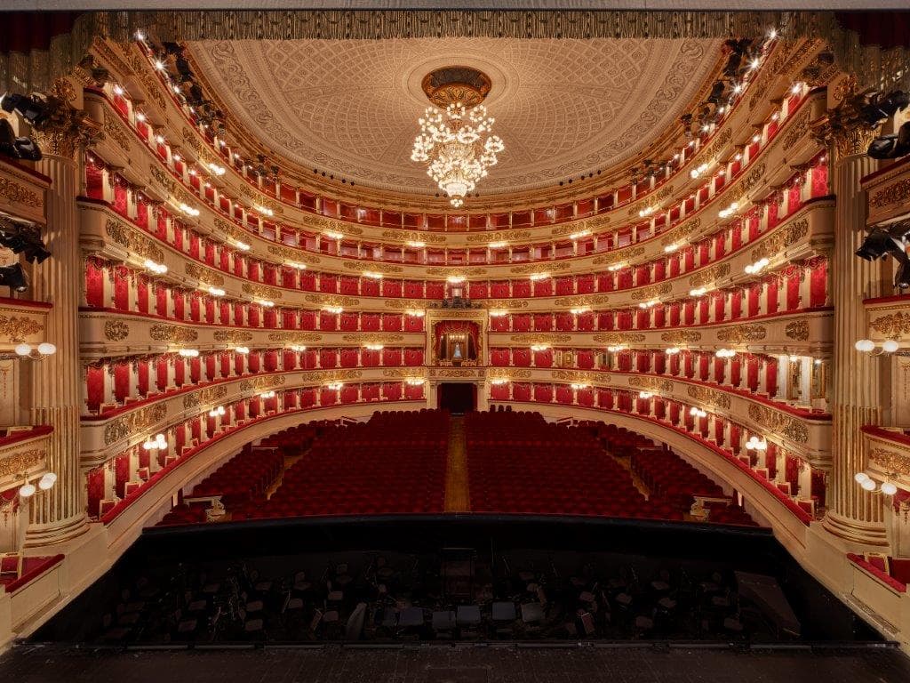 La foto mostra il teatro nella sua forma attuale, visto dal palcoscenico, senza artisti in scena e senza pubblico in platea e nei palchi. Oltre il palco, c’è la buca dell’orchestra con i leggii e le partiture. A seguire, la platea con le attuali poltrone di velluto rosso intenso, i cinque ordini di palchi e il loggione senza drappeggi, decorati con lo stesso velluto rosso intenso delle sedute in platea. Il lampadario, sostituito a quello dell’Ottocento dopo la Seconda Guerra Mondiale, ne replica l’aspetto originario.